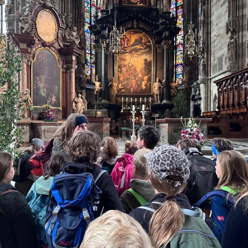 Eine Gruppe von Menschen mit Rucksäcken steht in einer Kirche und sieht ein Gemälde auf dem Altar.