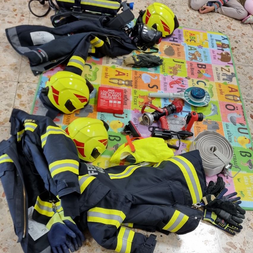 Eine Sammlung von Feuerwehrausrüstung, einschließlich Helme, Jacken, Handschuhe und Ausrüstung, ist auf einem bunten Alphabet-Matte ausgebreitet.
