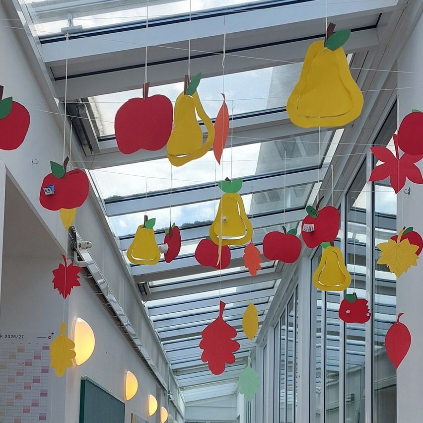Ein Flur mit einer Glasdecke ist mit hängenden Papierausschnitten von Äpfeln, Birnen und Blättern dekoriert.