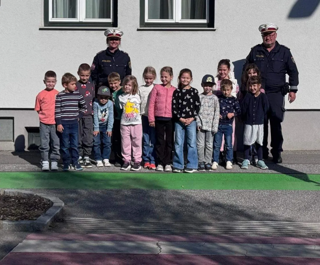 Eine Gruppe von Kindern und zwei Polizeibeamten stehen vor einem Gebäude. Die Kinder tragen verschiedenfarbige Kleidung und Schuhe.
