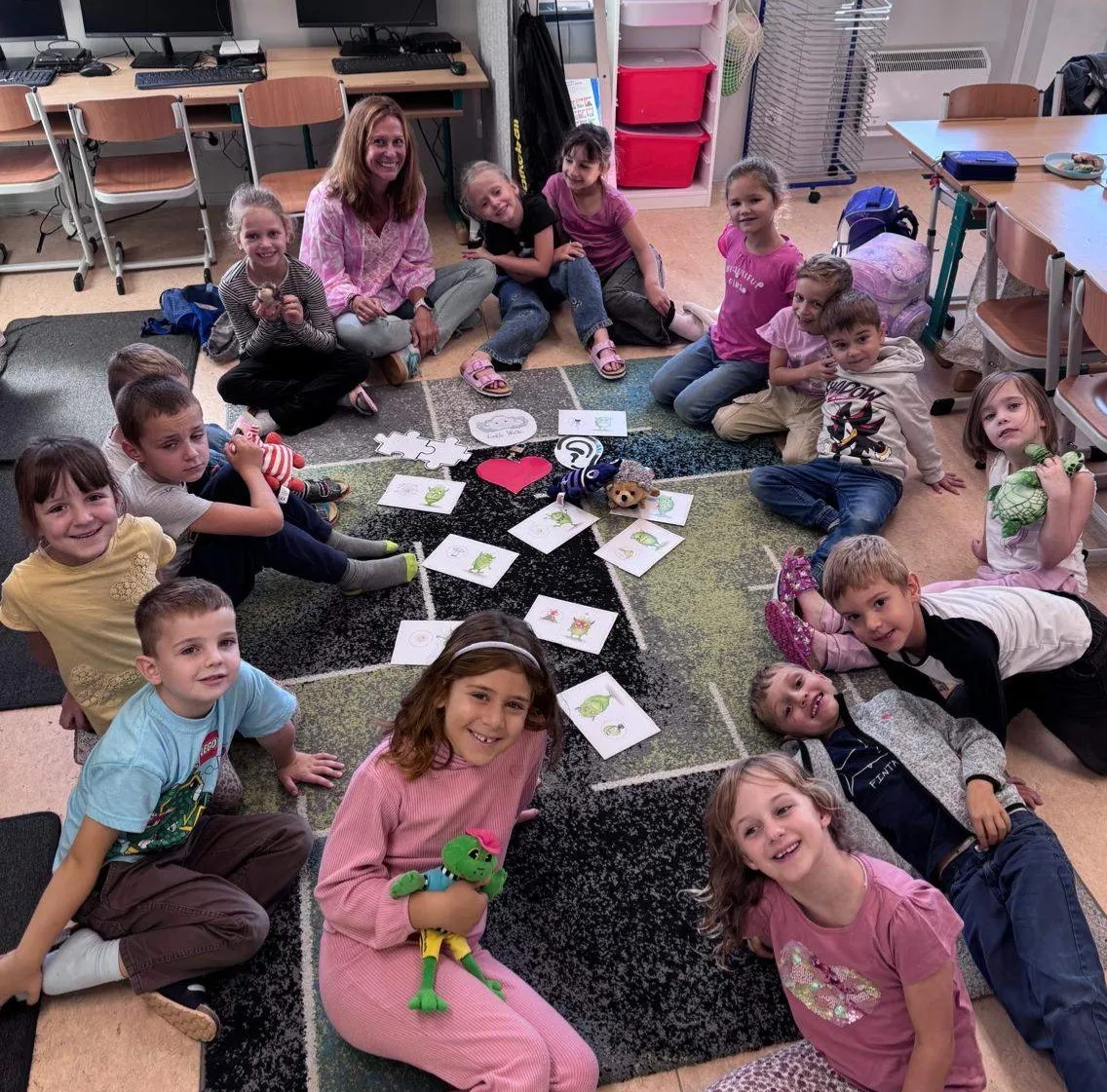Eine Gruppe von Kindern und einer Frau sitzen auf dem Boden in einem Klassenzimmer. Sie halten Spielzeug und betrachten Karten mit Bildern von Tieren.