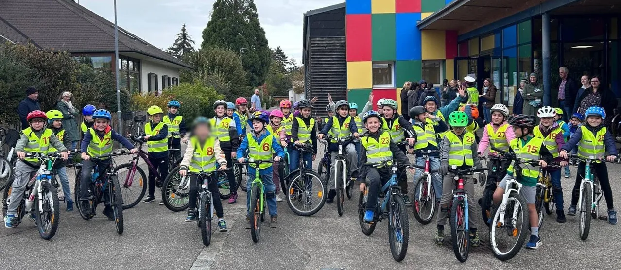 Eine Gruppe von Kindern, die gelbe Westen und Helme tragen, posiert für ein Foto vor einem farbenfrohen Gebäude.