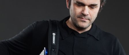 Ein Mann in einem schwarzen Hemd mit einem weißen Logo auf der linken Schulter schaut nach unten.