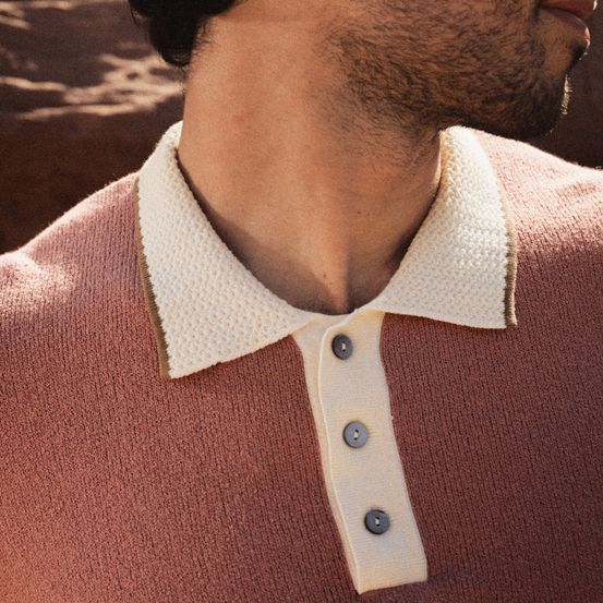 Ein Mann trägt ein gestricktes rosa Polohemd mit weißem Kragen und zwei Knöpfen vorne.