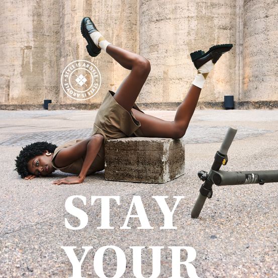 Eine Frau in Stiefeln liegt auf der Seite auf einem Betonblock, die Beine gebeugt und Arme ausgestreckt. Dahinter ist ein Metallobjekt zu sehen. Das Bild hat den Text 'BLEIB DEIN'.