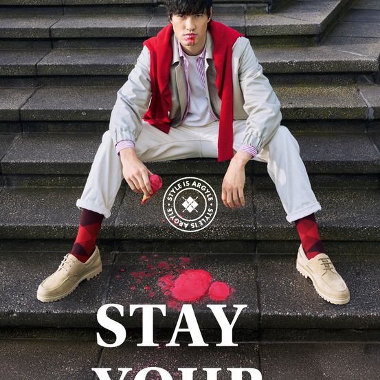 Ein Mann sitzt auf einer Treppe mit roter Farbe an seinen Schuhen und Lippen. Er hält einen Pinsel. Darunter stehen die Worte 'Bleiben Sie'.