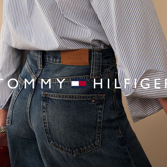 Ein Nahaufnahme von Tommy Hilfiger Jeans mit einem braunen Label auf der Gesäßtasche. Die Jeans haben einen roten Taschenanhänger mit dem Markenlogo.