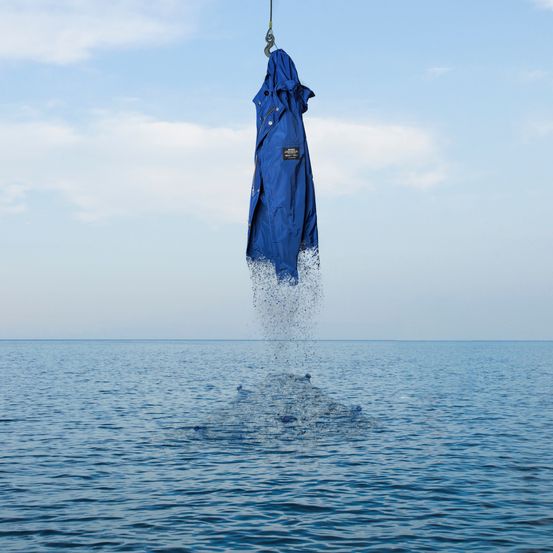 Ein blauer Mantel hängt an einem Haken über dem Ozean, wobei Wasser um ihn herum spritzt an einem sonnigen Tag.