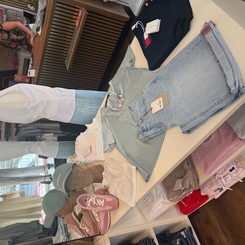 A clothing display with various items such as denim shorts, a white shirt, and sneakers on a wooden floor.