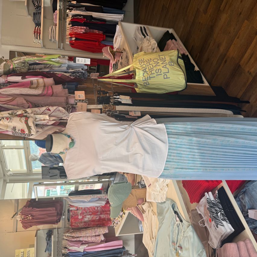 A clothing store with a variety of garments on display, including a white blouse with a blue skirt and a yellow bag with the text 'Because there is no planet B'.