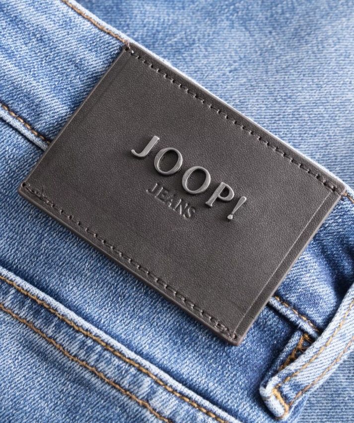 Ein Nahaufnahme eines schwarzen Lederetiketts mit dem Text 'JOOP! JEANS', das an einer Jeans mit blauer Farbe angebracht ist.