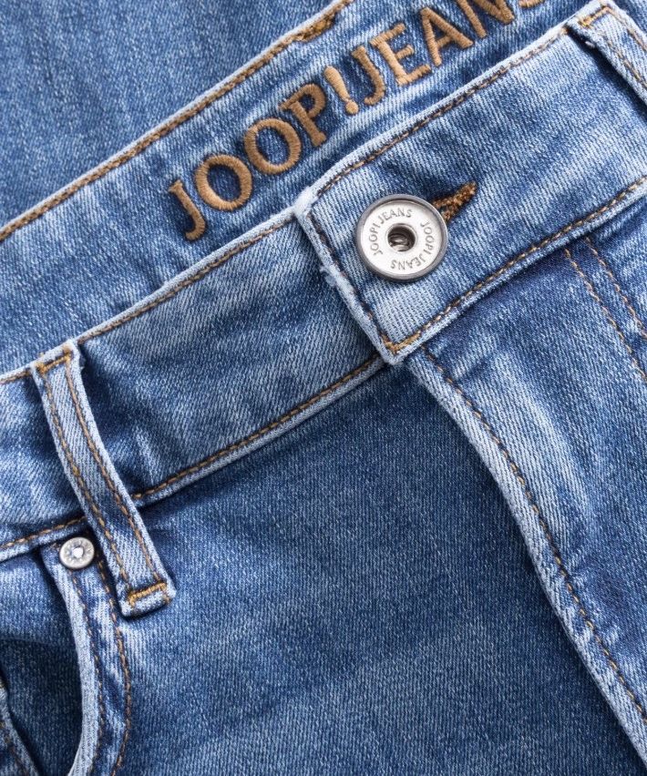 Eine Nahaufnahme von blauen Jeans mit der Marke 'JOOP!JEANS' auf der Gesäßtasche und einem silbernen Knopf auf der Vordertasche.