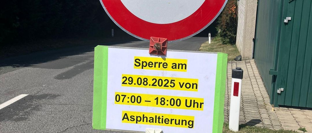 Ein Schild an einem Pfosten mit einem roten Kreis weist auf eine Straßensperrung für Asphaltarbeiten am 29.08.2025 von 07:00 bis 18:00 Uhr hin.