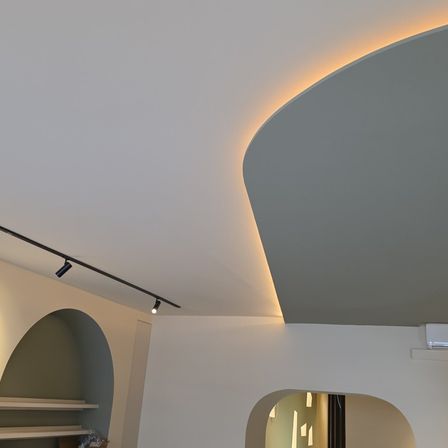 Ein Innenbereich mit gekrümmter Decke, Schienenbeleuchtung und gewölbten Nischen. Ein modernes, minimalistisches Design in Weiß und Grau.