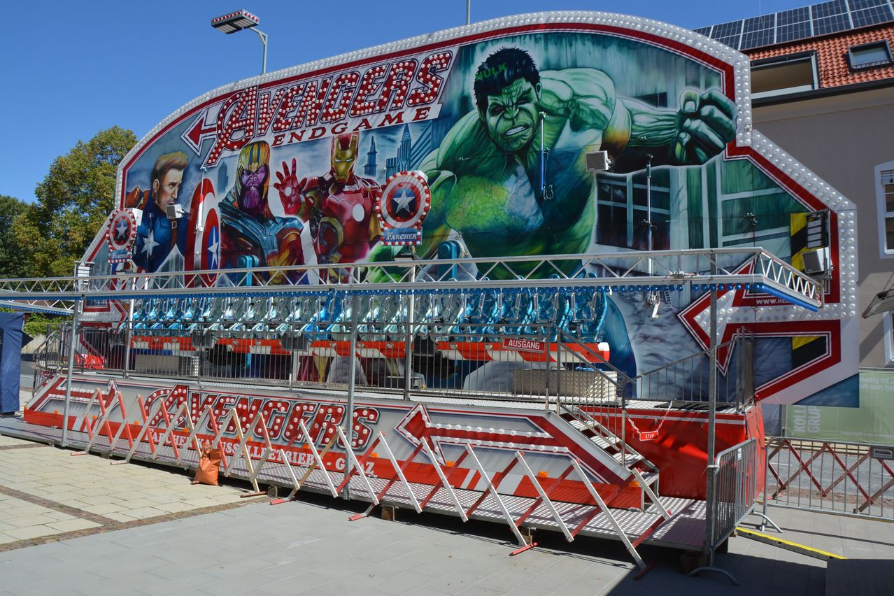 A colorful ride at an amusement park features a mural of Avengers characters, including Hulk, Iron Man, and Captain America. The ride has a metal railing and a staircase.