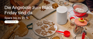 Ein Tisch mit Keksen auf einem Teller und einem Ausstecher. Ein Lautsprecher steht rechts und ein Messbecher links. Eine Hand einer Person liegt auf dem Tisch.