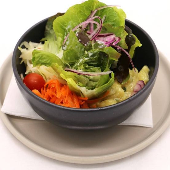 A bowl of salad with lettuce, carrots, and tomatoes on a white plate with a napkin.