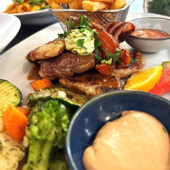 A plate with steak, vegetables, and sauces. French fries in a basket.