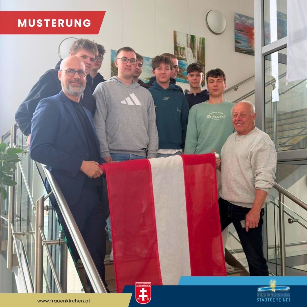 Eine Gruppe von Männern steht auf einer Treppe mit einer rot-weißen Flagge. Ein Mann hält die Flagge und lächelt. Über ihnen befindet sich ein rotes Banner mit weißem Text, das 'MUSSTERUNG' besagt.