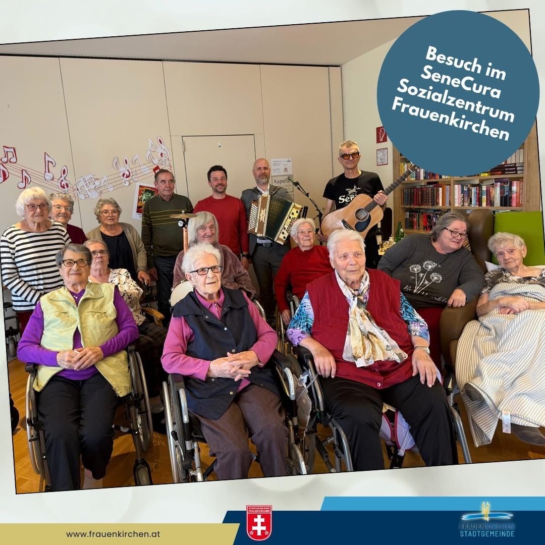 Eine Gruppe älterer Menschen, einige in Rollstühlen, versammelt sich in einem Raum. Musiknoten schmücken die Wand. Ein Mann spielt Akkordeon und ein anderer Gitarre. Der Raum ist mit Stühlen und Büchern gefüllt.