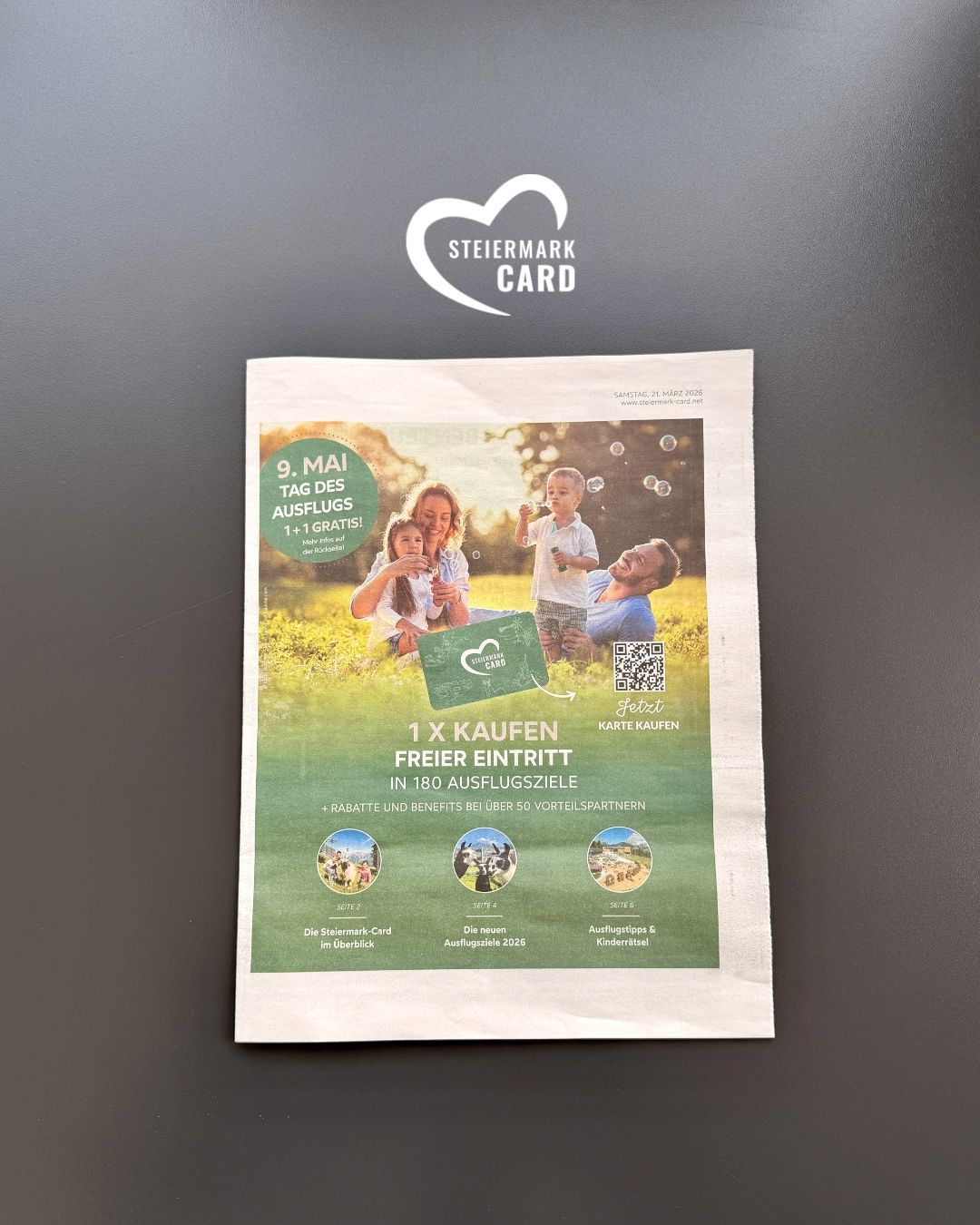 Plakat für die Stiermark Card. Es zeigt eine Familie, die einen Tag im Park genießt, mit einer grünen Karte sichtbar. Es bietet 1 kostenlosen Eintritt für den Kauf von 180 Tickets. Es gibt einen QR-Code und einige Symbole. Datum ist 9. Mai 2026.
