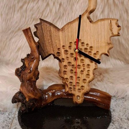 Eine handgefertigte Holzuhr mit einzigartigem Design, geformt wie ein Ast mit Karteneinlage und roter Sekundenzeiger. Sie ruht auf einer schwarzen Basis.