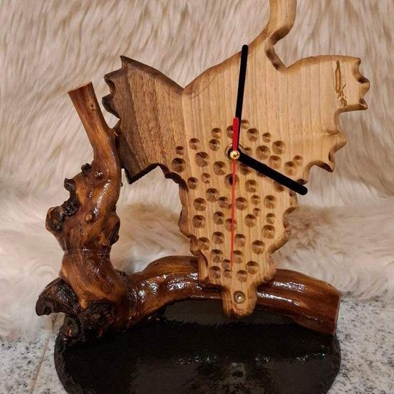 Eine handgefertigte Holzuhr mit einzigartigem Design, geformt wie ein Ast mit Karteneinlage und roter Sekundenzeiger. Sie ruht auf einer schwarzen Basis.