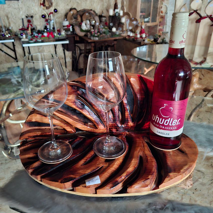 Ein Holztablett mit zwei Weingläsern und einer Flasche Rotwein darauf. Das Tablett hat ein Spiraldesign. Das Weinglas ist leer und die Flasche ist beschriftet.
