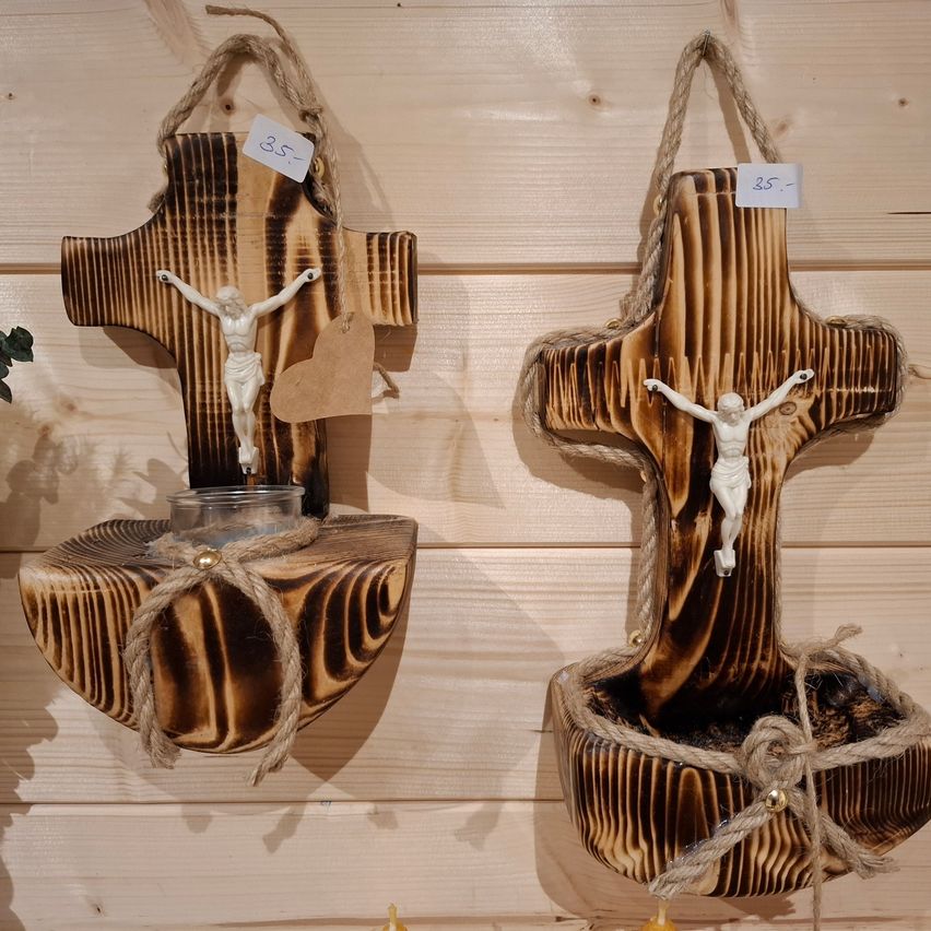Zwei Holzkreuze mit Kruzifix und Kerzenhalter hängen an einer Holzwand. Die Kreuze haben Seil und ein Herz.