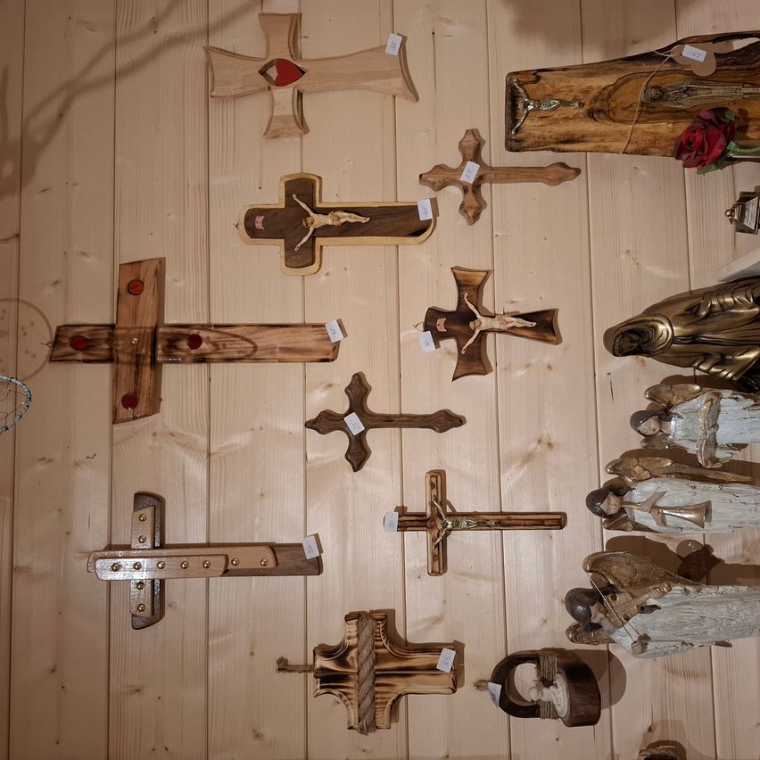 Eine Holzwand, geschmückt mit verschiedenen Holzkreuzen, einem hölzernen Kruzifix und einer hölzernen Statue einer Person mit einer Rose darauf.