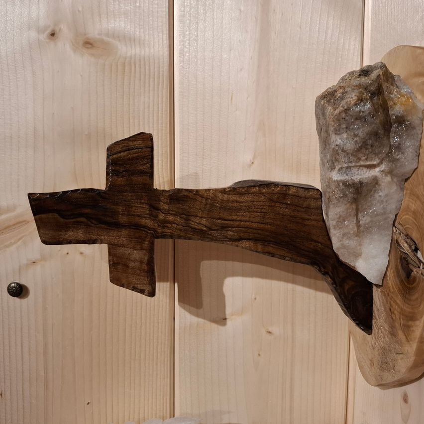 Ein holzernes Kreuz mit einem Kristall darauf ist an einer Holzwand befestigt.