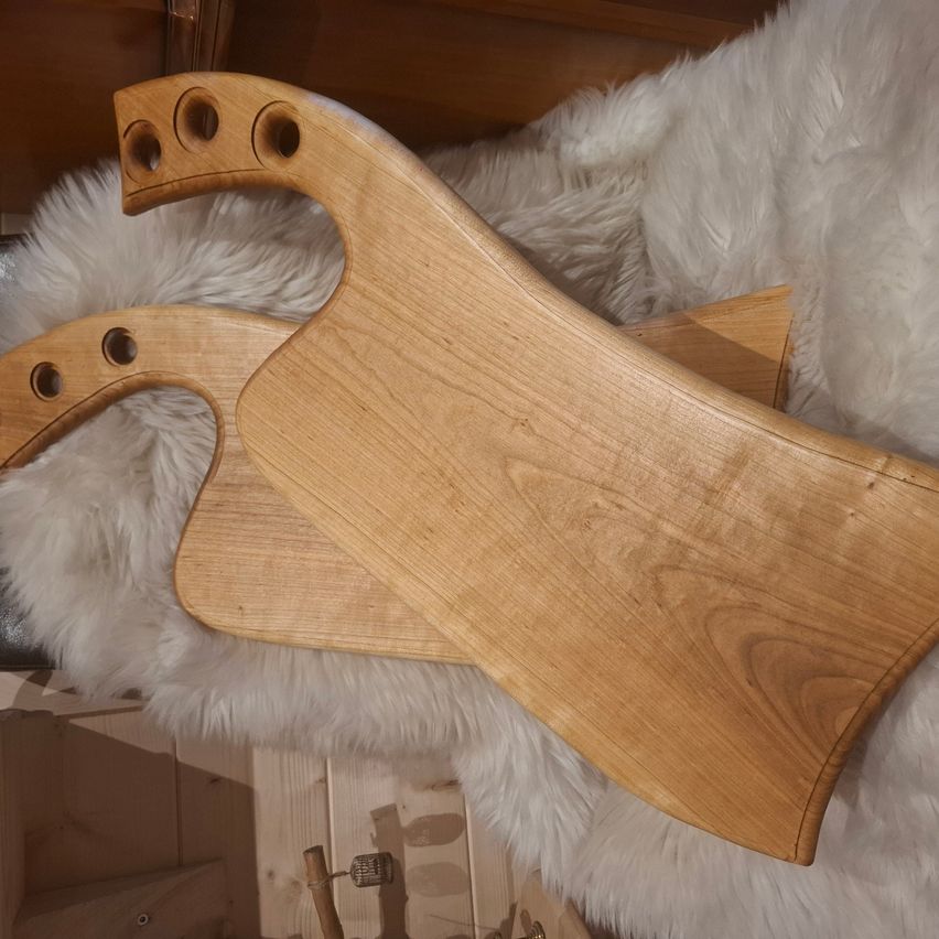 Ein Holzschneidebrett mit Griff liegt auf einer weißen Felloberfläche. Das Brett hat mehrere Löcher zum Aufhängen oder zur Aufbewahrung.