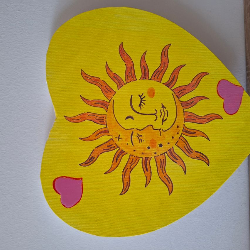 Ein herzförmiges Kunstwerk zeigt eine lächelnde Sonne mit gelben Strahlen. Die Sonne hat ein Kreuz in der Mitte und zwei Herzen auf beiden Seiten. Der Hintergrund ist leuchtend gelb.
