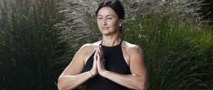 Eine Frau in schwarz-goldenen Yogahosen und einem ärmellosen Oberteil praktiziert Yoga auf einer Kiesfläche.