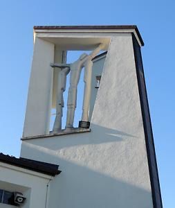 Ein hoher weißer Turm mit schwarzem Dach und einem Bogenfenster, mit einer Statue von zwei Personen im Inneren. Ein kleines Fenster und eine Überwachungskamera befinden sich auf der linken Seite.