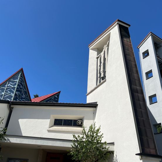 Ein weißes Kirchengebäude mit einem dreieckigen Dach und einem Glockenturm mit einer Statue.