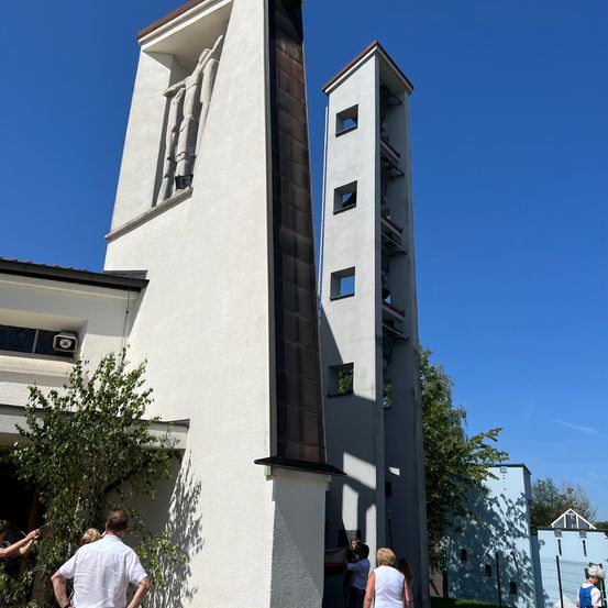 Ein modernes Kirchengebäude unter einem klaren blauen Himmel mit zwei hohen Glockentürmen, Menschen sind in der Nähe des Eingangs versammelt.
