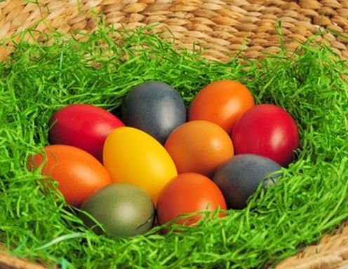 Ein Weidenkorb voller bunter Ostereier auf einem Bett aus grünem Gras.