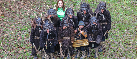 Eine Gruppe von Menschen in Hörnerkostümen steht auf einem Rasen. Eine Frau in einem grünen Shirt steht unter ihnen. Ein kleiner Junge hält ein Schild.