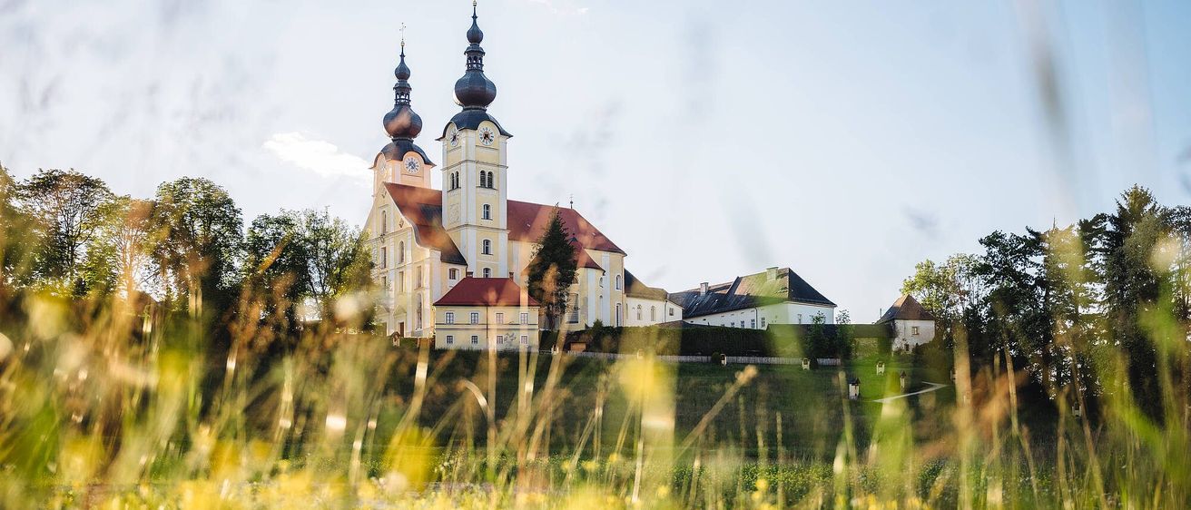 Eine große Kirche mit zwei Kuppeln und zwei Uhren steht auf einem Hügel unter einem klaren Himmel.