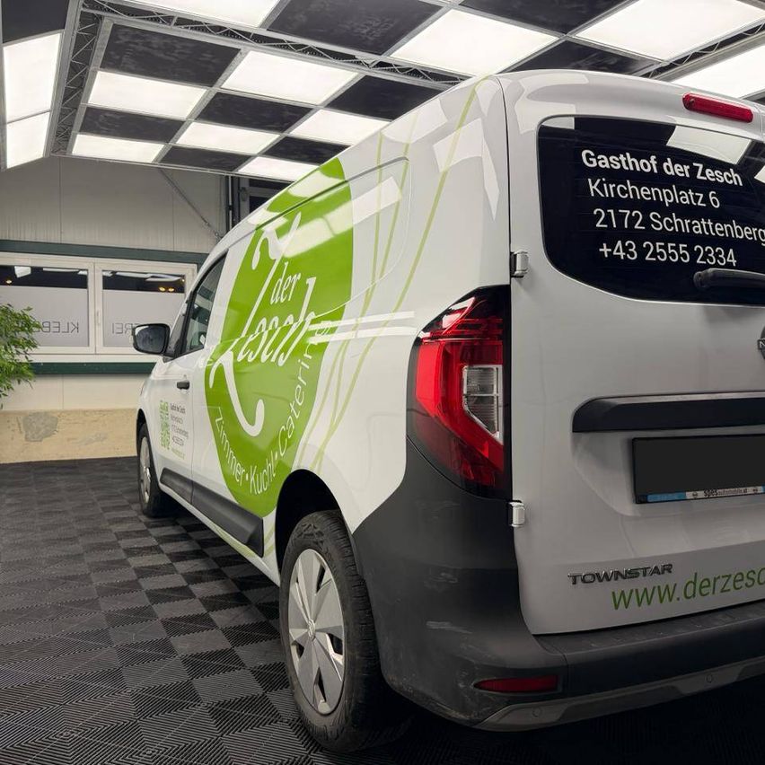 Ein weißer und grüner Lieferwagen mit Logo an der Seite und hinten, geparkt in einer Garage mit einem Schachbrettboden.