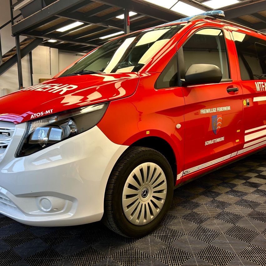 Ein roter Mercedes-Benz-Van, Modell AT05-MT, steht in einer Garage. Er ist mit MTFA und Freiwillige Feuerwehr gekennzeichnet.