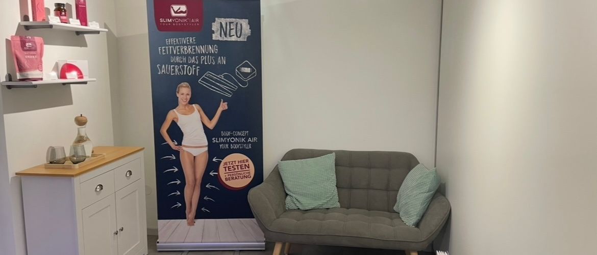 Ein Zimmer mit einer Couch, einem Tisch und einem großen Plakat einer Frau, die ein Produkt für effektives Fettverbrennen bewirbt.