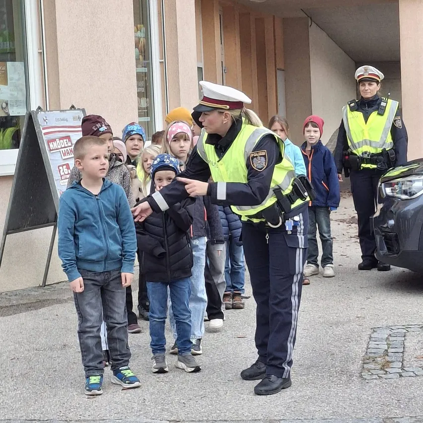 Eine Polizistin spricht mit einer Gruppe von Kindern, von denen eines eine blaue Jacke trägt.