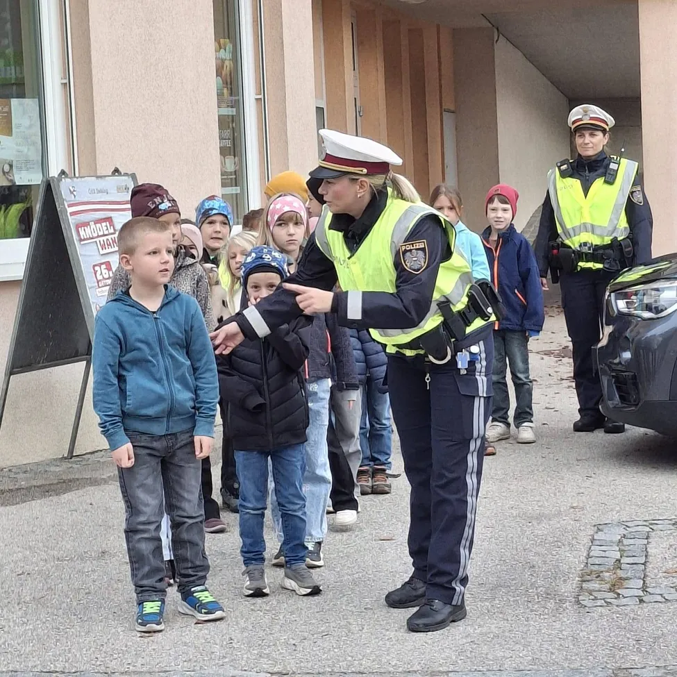 Eine Polizistin spricht mit einer Gruppe von Kindern, von denen eines eine blaue Jacke trägt.
