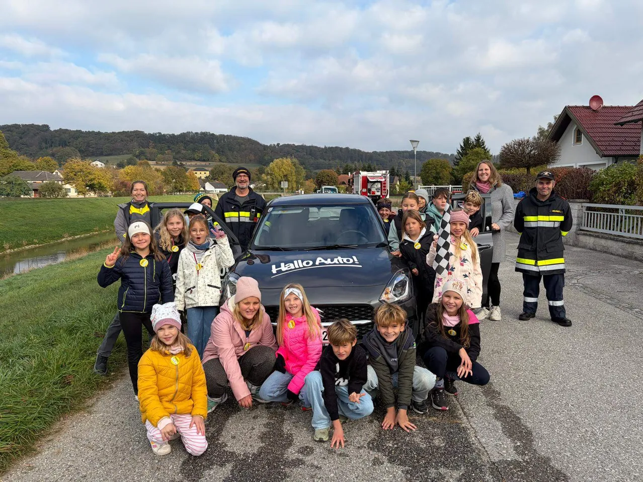 Eine Gruppe von Kindern und Erwachsenen posiert für ein Foto vor einem Auto mit der Aufschrift 'Hallo Auto!' auf der Motorhaube.