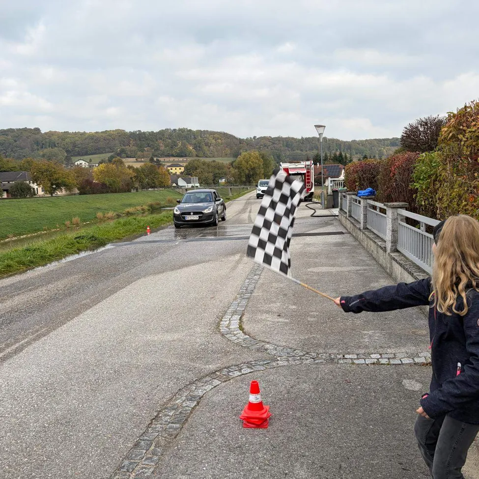 Ein junges Mädchen steht am Straßenrand und hält eine schwarz-weiß karierte Flagge, während ein Auto an ihr vorbeifährt.