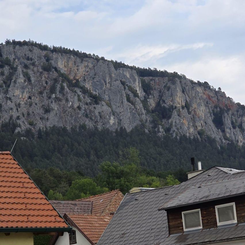 Ein Blick auf einen felsigen Berg mit ein paar Häusern im Vordergrund, eines mit einem roten Dach und ein anderes mit einem grauen Dach.