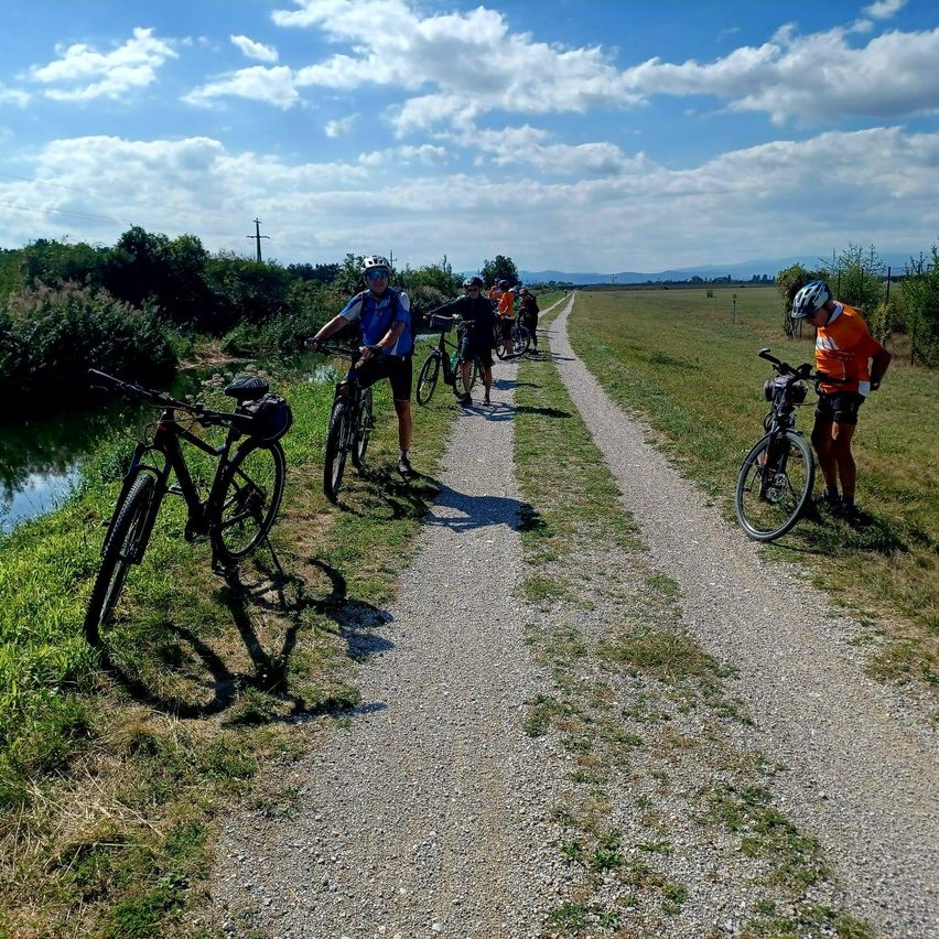 Eine Gruppe von Radfahrern fährt auf einem Schotterweg in der Nähe eines Flusses, mit Helmen und Fahrrädern.