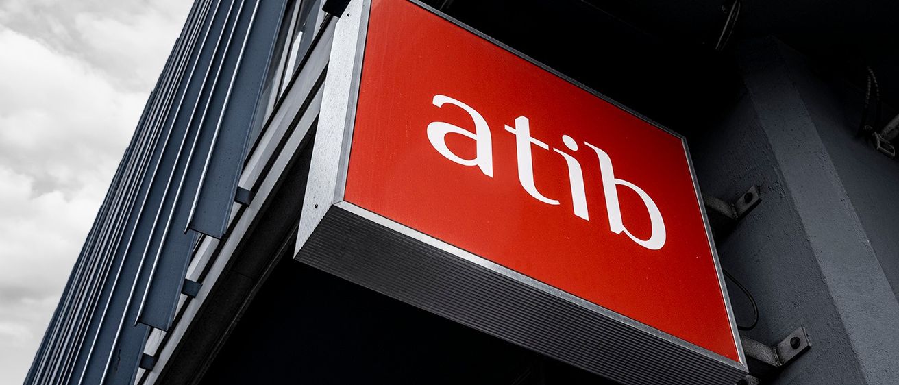 Ein rotes Schild mit dem Wort 'atib' ist an einem modernen Gebäude mit grauer Fassade angebracht. Das Schild ist prominent platziert und zeigt wahrscheinlich den Namen des Gebäudes oder einer Organisation an.